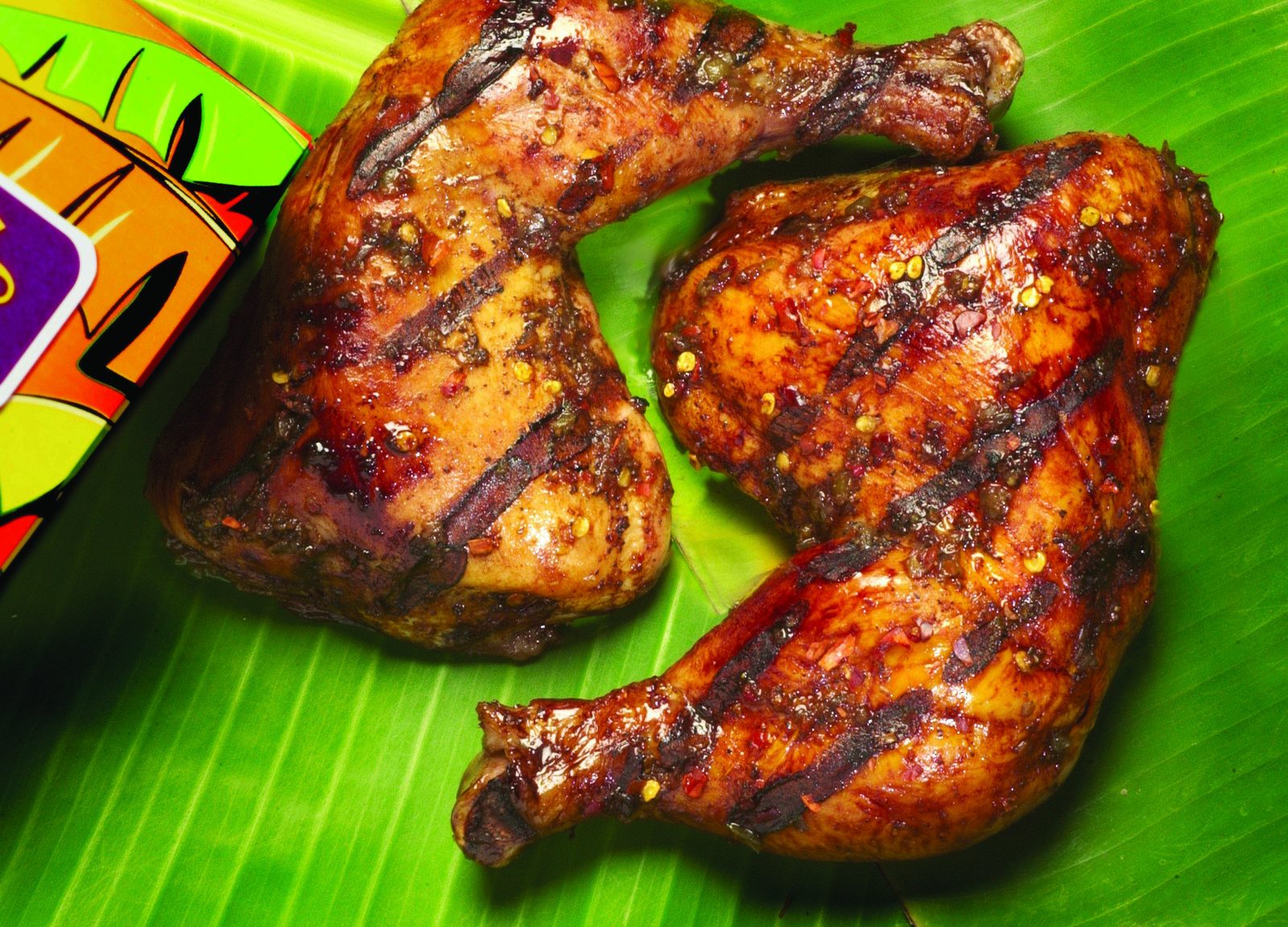 Fire-grilled jerk chicken leg quarters on a banana leaf